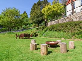 A garden with wooden stools around a fire pit and a wooden table with chairs near a stone wall at The Woodlands in Berrynarbor