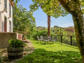 An outdoor patio area with metal chairs and table on grass near a tree and a house at The Woodlands in Berrynarbor