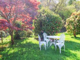 A garden with a white metal table and four chairs surrounded by trees and bushes at The Woodlands in Berrynarbor