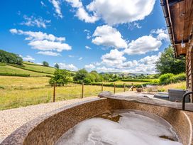 A hot tub overlooking a grass field and hills at Birch Banc Retreats - Bedw Llanidloes