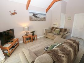 A living room with two sofas a television on a wooden stand a lamp and a painting of a boat at Love Cottage in Tenby