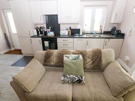 A kitchen with white cabinets black countertop a sofa with cushions and blankets at Love Cottage in Tenby