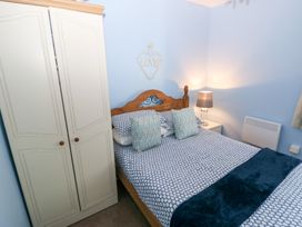 A bedroom with a wooden bed with patterned bedding and pillows a white wardrobe and a bedside table with a lamp at Love Cottage Tenby