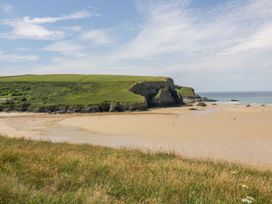 A sandy beach with grassy cliffs and the ocean at 49 Atlantic Reach in Newquay