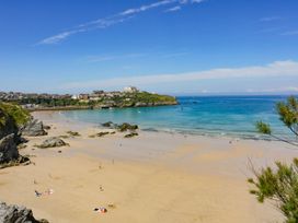 A sandy beach with people walking and sitting near the ocean with houses on a hill in the background at 49 Atlantic Reach in Newquay