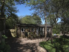 A wooden building surrounded by trees and gravel at Orchard Lodge in Bolney