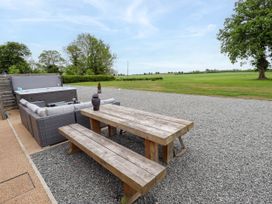 An outdoor seating area with a wooden picnic table wooden bench cushioned wicker sofa and hot tub on a gravel surface with grass and trees in the background at Pheasant's Roost in Lelley near Burton Pidsea
