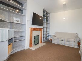 A living room with a television, shelf, sofa, and fireplace at The Three Tees in Newquay