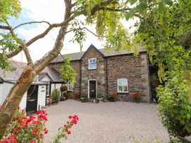 A stone house with a black door and windows surrounded by a gravel courtyard and plants at Pen Y Bont in Llanfair Talhaiarn