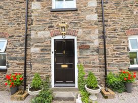 The front door of a stone house with plants in pots and a lantern above the door at Pen Y Bont in Llanfair Talhaiarn