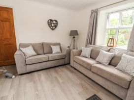 A living room with two beige sofas and patterned cushions a wooden door and a window with curtains at Pen Y Bont in Llanfair Talhaiarn