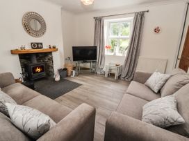A living room with two sofas facing a wood burning stove and a television near a window at Pen Y Bont in Llanfair Talhaiarn