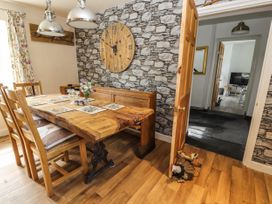 A dining room with a wooden table and chairs a stone patterned wall with a large clock and an open door showing a hallway at Pen Y Bont in Llanfair Talhaiarn