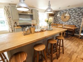 A kitchen with a wooden island and stools and a dining table with chairs against a stone patterned wall at Pen Y Bont in Llanfair Talhaiarn