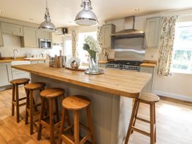A kitchen with a wooden island and five stools with beige cabinets and floral curtains at Pen Y Bont in Llanfair Talhaiarn