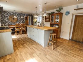 Kitchen with wooden floor island counter with stools dining table and chairs against stone patterned wall at Pen Y Bont in Llanfair Talhaiarn