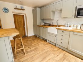 A kitchen with wooden floors grey cabinets a wooden stool a clock and countertop appliances at Pen Y Bont in Llanfair Talhaiarn
