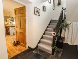 A stairway with carpeted steps and a handrail decorated with plants next to a wooden door leading to a kitchen with stools at Pen Y Bont in Llanfair Talhaiarn