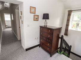 A hallway with a wooden dresser and lamp near stairs and a window with plaid curtains at Pen Y Bont in Llanfair Talhaiarn