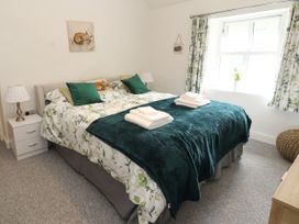 A bedroom with a double bed with green and white bedding bedside tables with lamps and a window with floral curtains at Pen Y Bont in Llanfair Talhaiarn