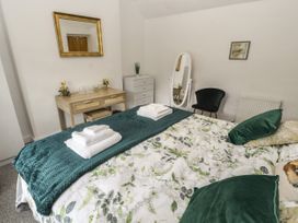 A bedroom with a bed with green and floral bedding a wooden desk with small decorations a white chest of drawers a black chair a standing mirror and a wall mirror at Pen Y Bont in Llanfair Talhaiarn