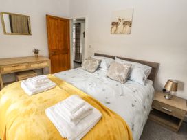 A bedroom with a bed covered by a yellow blanket and white towels with a wooden door small desk with a mirror and side table with a lamp and painting on the wall at Pen Y Bont in Llanfair Talhaiarn