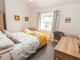 A bedroom with a bed covered with white and yellow bedding a wooden desk a chair and two framed pictures on the wall at Pen Y Bont in Llanfair Talhaiarn