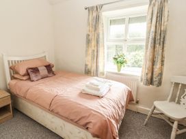 A bedroom with a single bed pink bedding folded towels on bed a window with curtains and a white chair at Pen Y Bont in Llanfair Talhaiarn