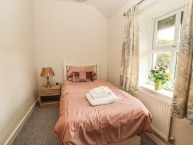A bedroom with a single bed a nightstand with a lamp a window with curtains and a flower pot at Pen Y Bont in Llanfair Talhaiarn