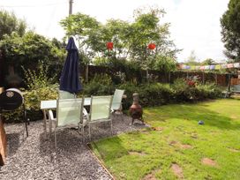 A garden with a glass table and chairs on gravel a blue umbrella a barbecue and a chiminea at Pen Y Bont in Llanfair Talhaiarn