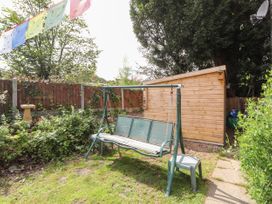 A garden with a swing seat a plastic chair and a wooden shed in the background at Pen Y Bont in Llanfair Talhaiarn
