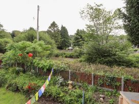 A garden with plants flowers and prayer flags next to a wooden fence with trees and a utility pole in the background at Pen Y Bont in Llanfair Talhaiarn