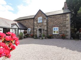 A gravel courtyard with red flowers in pots outside a stone house at Pen Y Bont in Llanfair Talhaiarn