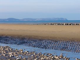 A sandy beach with ripples and rocks near the shore with a body of water and hills in the distance at Pen Y Bont in Llanfair Talhaiarn