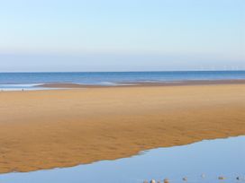A sandy beach with shallow water and wind turbines visible on the horizon at Pen Y Bont in Llanfair Talhaiarn