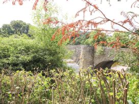 A stone bridge over a river surrounded by green trees and plants at Pen Y Bont in Llanfair Talhaiarn