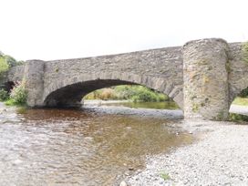 A stone arch bridge over a shallow river with a rocky shore at Pen Y Bont in Llanfair Talhaiarn