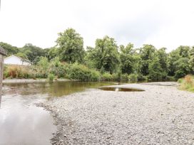 A river with a rocky shore and green trees along the bank near a white house at Pen Y Bont in Llanfair Talhaiarn