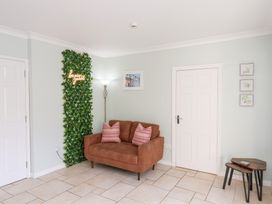 A room with a brown sofa with two striped pillows a tall floor lamp a green leafy wall decoration with neon sign a wooden nesting table and three framed pictures on a light wall at North Beach Lodge in Scarborough