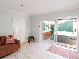 A room with a brown sofa and pillow next to a white door and small tables beside sliding glass doors leading to an outdoor hot tub at North Beach Lodge in Scarborough