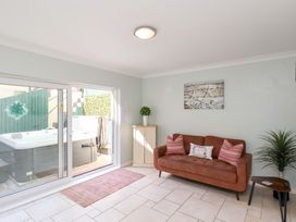 A room with a brown sofa with pillows a small cabinet a potted plant sliding glass door leading to a hot tub outside at North Beach Lodge in Scarborough