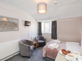 A bedroom with a bed, two grey armchairs, a small wooden table, a wall-mounted tv, a mirror, and a window with dark curtains at North Beach Lodge in Scarborough