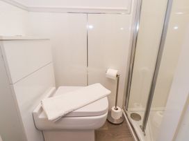 A bathroom with a toilet holding a white towel next to a toilet paper holder and a glass shower door at North Beach Lodge in Scarborough