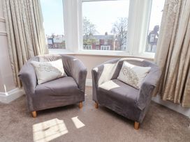 Two gray armchairs with decorative cushions next to large windows with curtains at North Beach Lodge in Scarborough