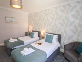 A bedroom with two single beds with green throws and pillows bedside tables with lamps and a gray armchair at North Beach Lodge in Scarborough