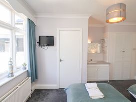 A bedroom with a bed, wall-mounted TV, window with blue curtains, sink area, and a closet at North Beach Lodge in Scarborough