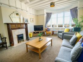 A living room with a fireplace a wooden coffee table a gray sofa and armchair a yellow chair a television and a bay window at Westbourne in Llandudno