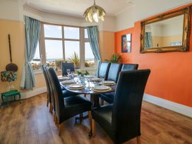 A dining room with a set table around a wooden table and black chairs with large windows and light blue curtains at Westbourne in Llandudno