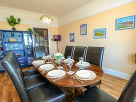 A dining room with a wooden table set with plates glasses and cutlery and black leather chairs a blue cabinet with plants and decorations and framed pictures on a beige wall at Westbourne in Llandudno