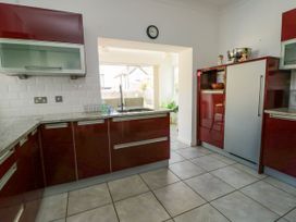 A kitchen with red cabinets a sink a clock on the wall and a window showing outdoor view at Westbourne in Llandudno